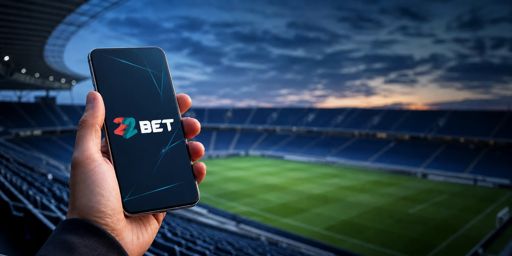 Mano sosteniendo un teléfono con la aplicación de 22BET frente a un estadio